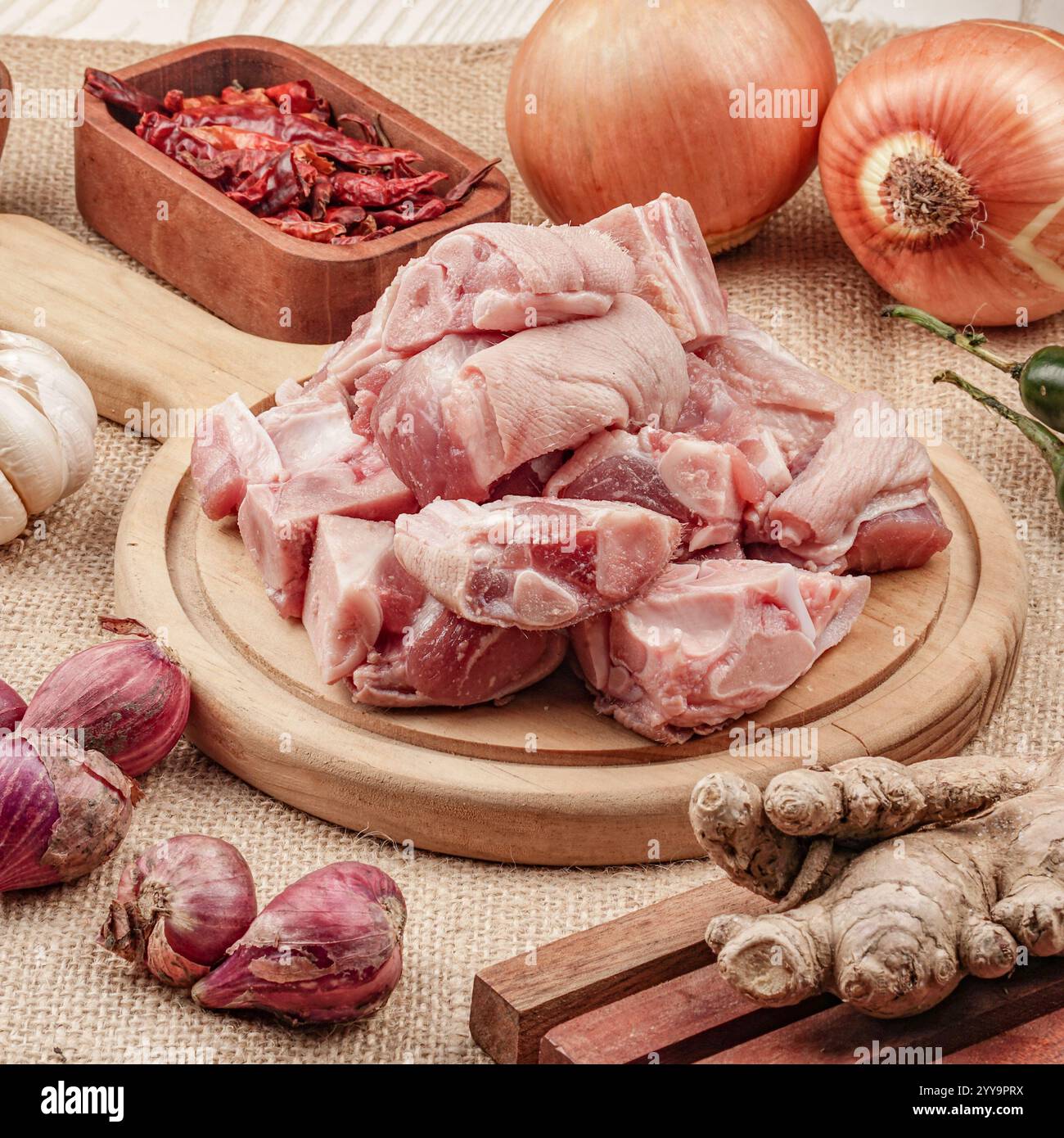 Carne di capra tritata fresca su una tavola di legno circondata da ingredienti tradizionali come zenzero, cipolle, aglio e peperoncini secchi Foto Stock