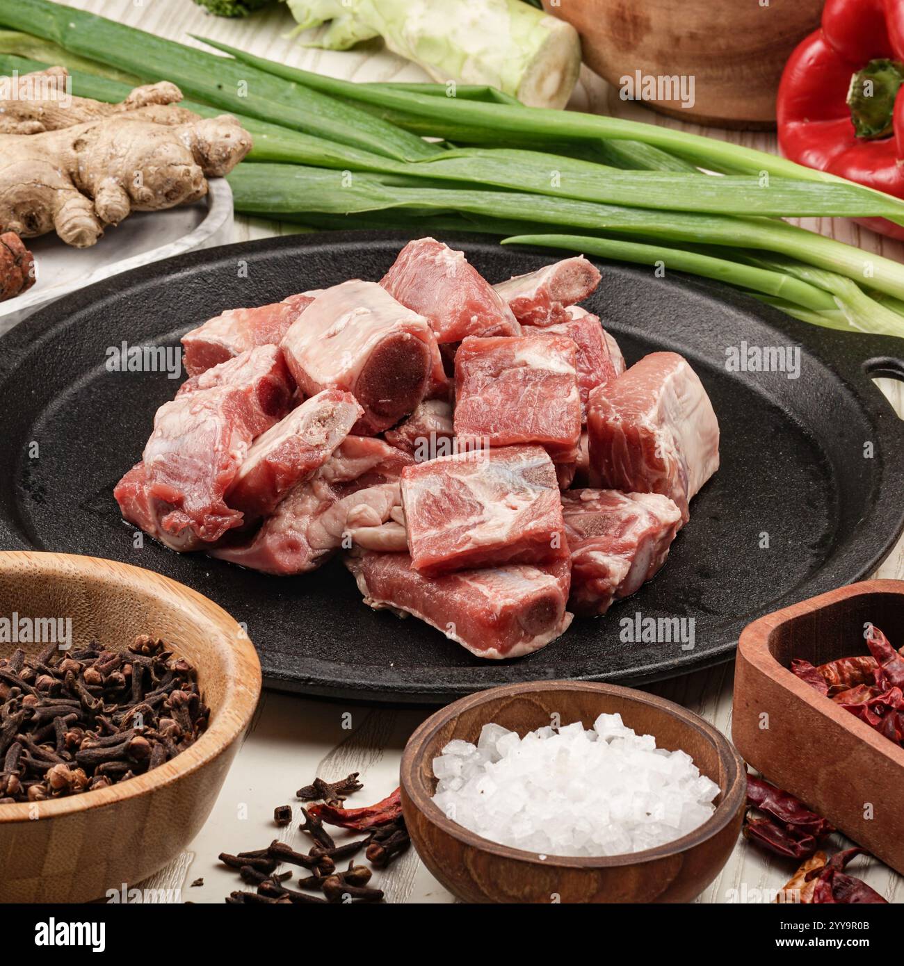 Costolette di maiale fresche con osso disposte su un piatto di ghisa circondato da spezie e verdure aromatiche, preparate perfettamente per un sostanzioso stufato fatto in casa Foto Stock
