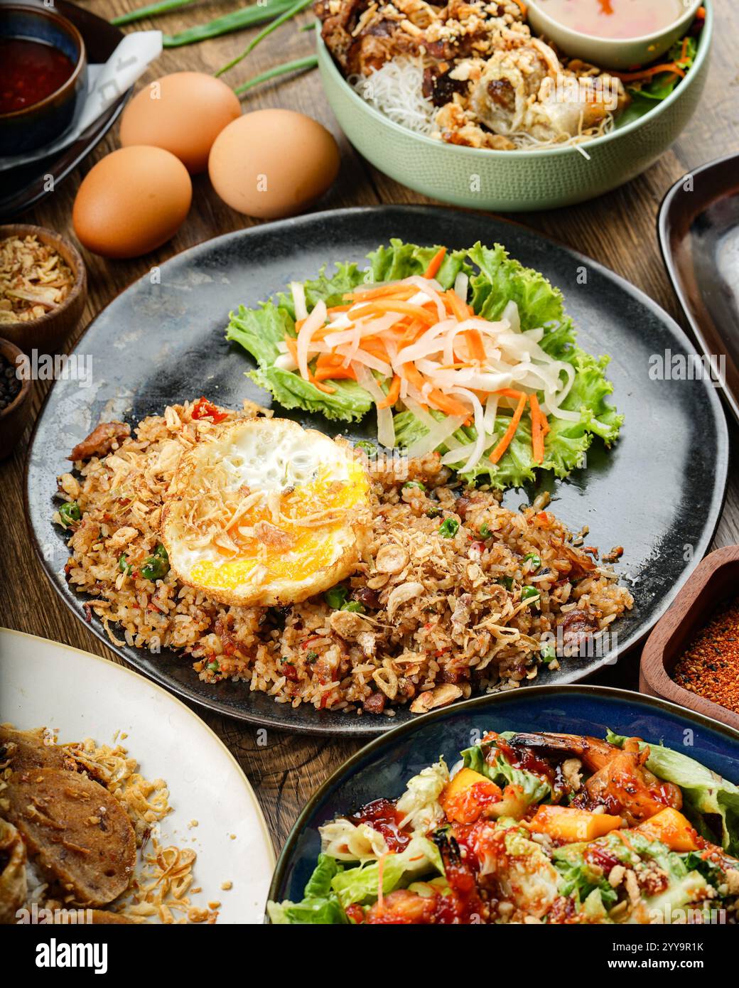 Un abbondante piatto di riso fritto in stile vietnamita condito con un uovo croccante dorato, verdure sott'aceto e scalogni fritti profumati, servito con contorni vivaci Foto Stock