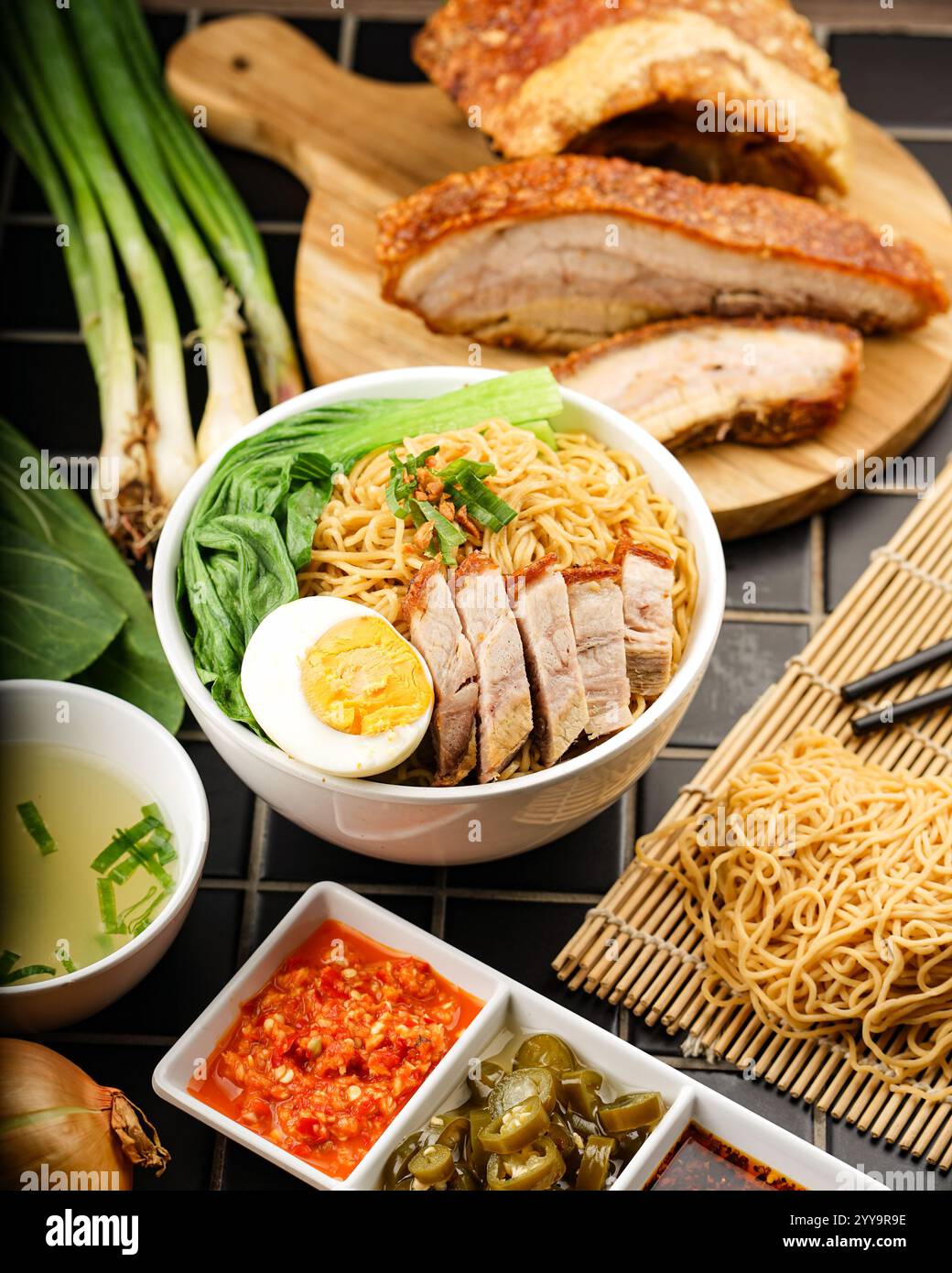 Un saporito recipiente di noodle all'uovo secco in stile filippino ricoperto di pancetta di maiale croccante, bok choy, uovo bollito e guarnito con scaldini e pezzi di aglio. Foto Stock