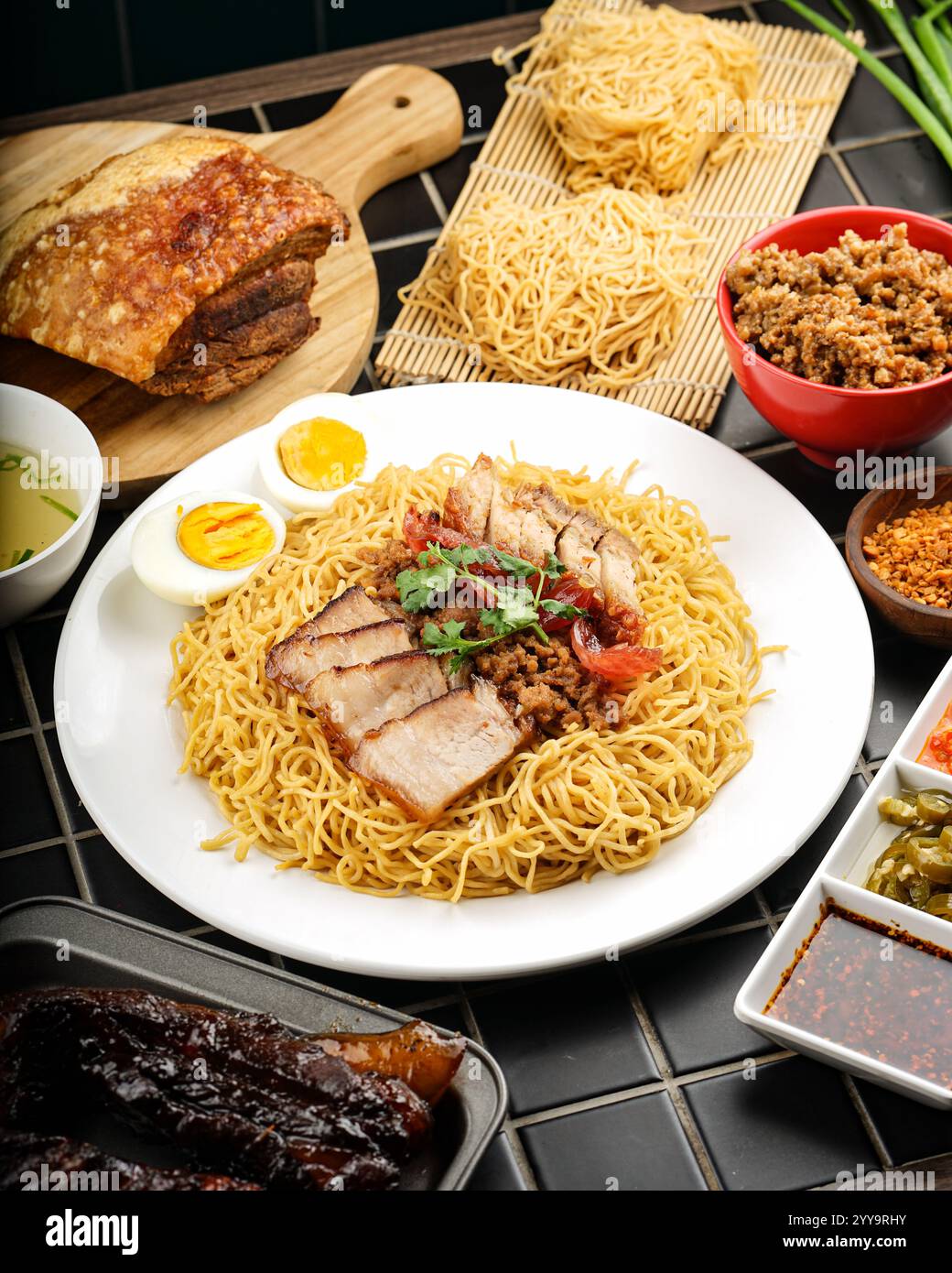 Spaghetti all'uovo cotti a secco con pancetta di maiale croccante, char siu, maiale macinato e un uovo sodo, circondati da spaghetti all'uovo freschi, brodo ricco e salse Foto Stock