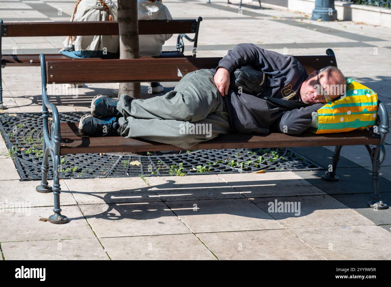 Budapest, Ungheria - 17 settembre 2024: Povero senzatetto che dorme su una panchina in piazza Szell Kalman a Budapest, Ungheria, in tono drammatico. Alti quali Foto Stock