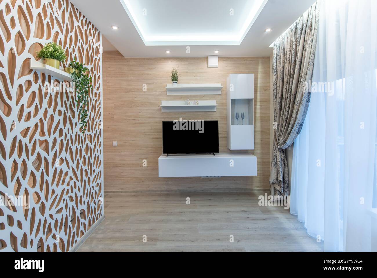 Un soggiorno contemporaneo con una parete in legno, TV montata, elementi di arredo eleganti, tende a motivi geometrici, design accattivante per un comfort confortevole Foto Stock