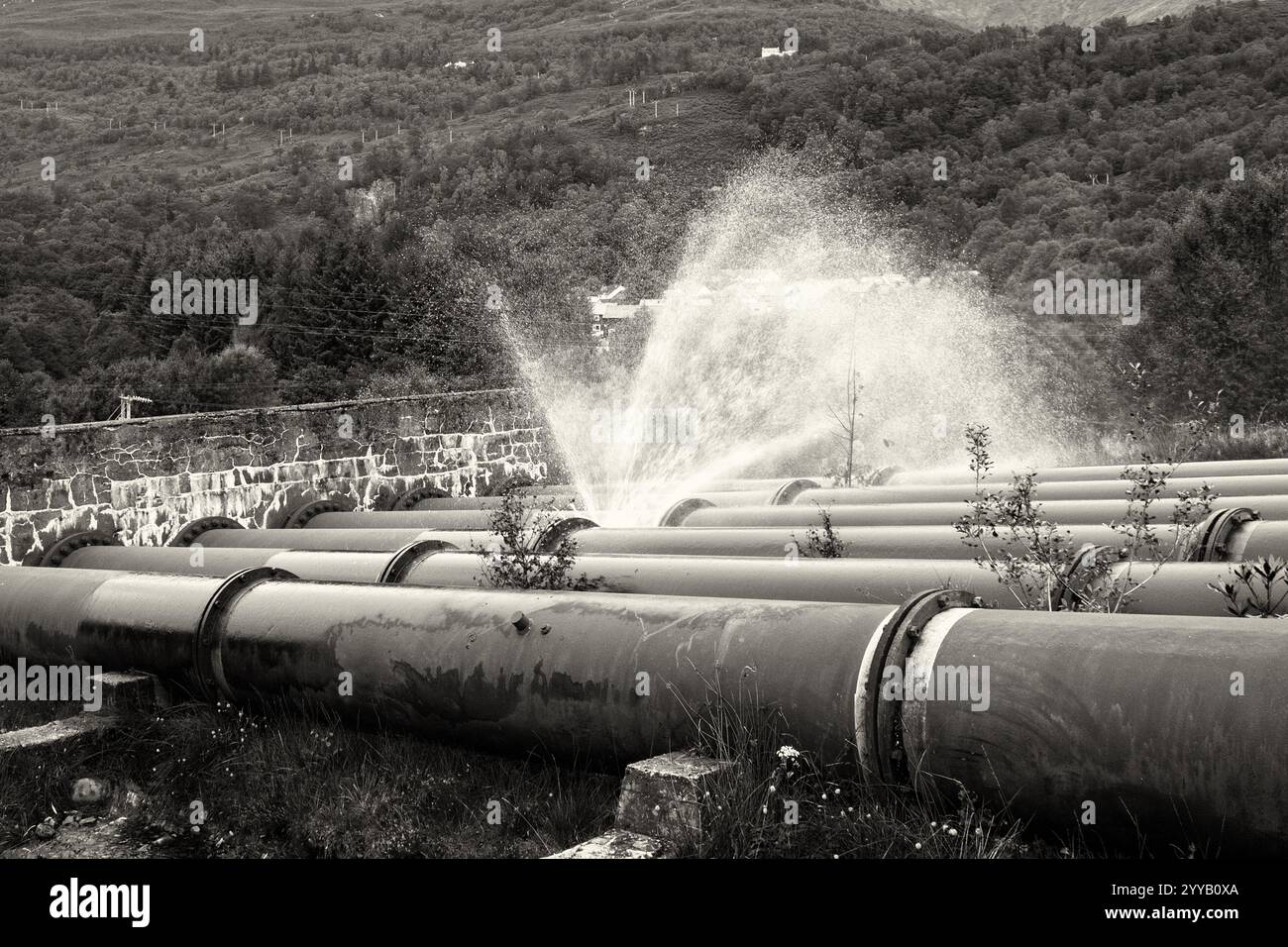 Primo piano bianco e nero dell'acqua che fuoriesce da una flangia che perde negli enormi tubi di ferro che alimentano la centrale idroelettrica Kinlochleven Foto Stock