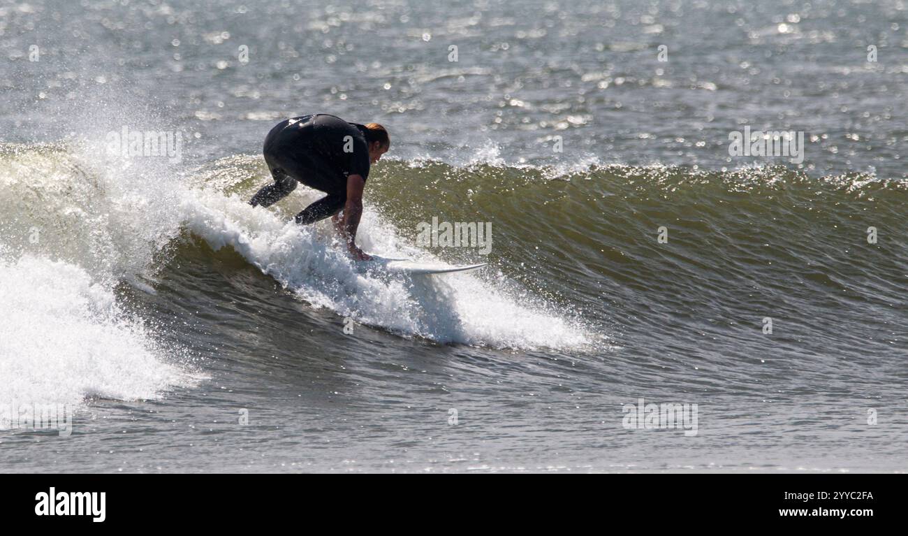 Gilgo Beach, New York, USA - 31 agosto 2023: Un surfista salta sapientemente sulla tavola mentre cavalca una grande onda in spiaggia durante il giorno. Foto Stock