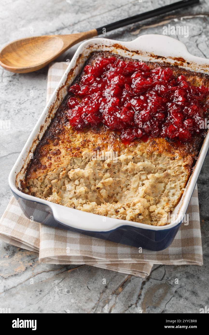 Casseruola finlandese Maksalaatikko a base di riso e fegato con primo piano di salsa di mirtilli rossi sulla teglia da forno sul tavolo. Verticale Foto Stock