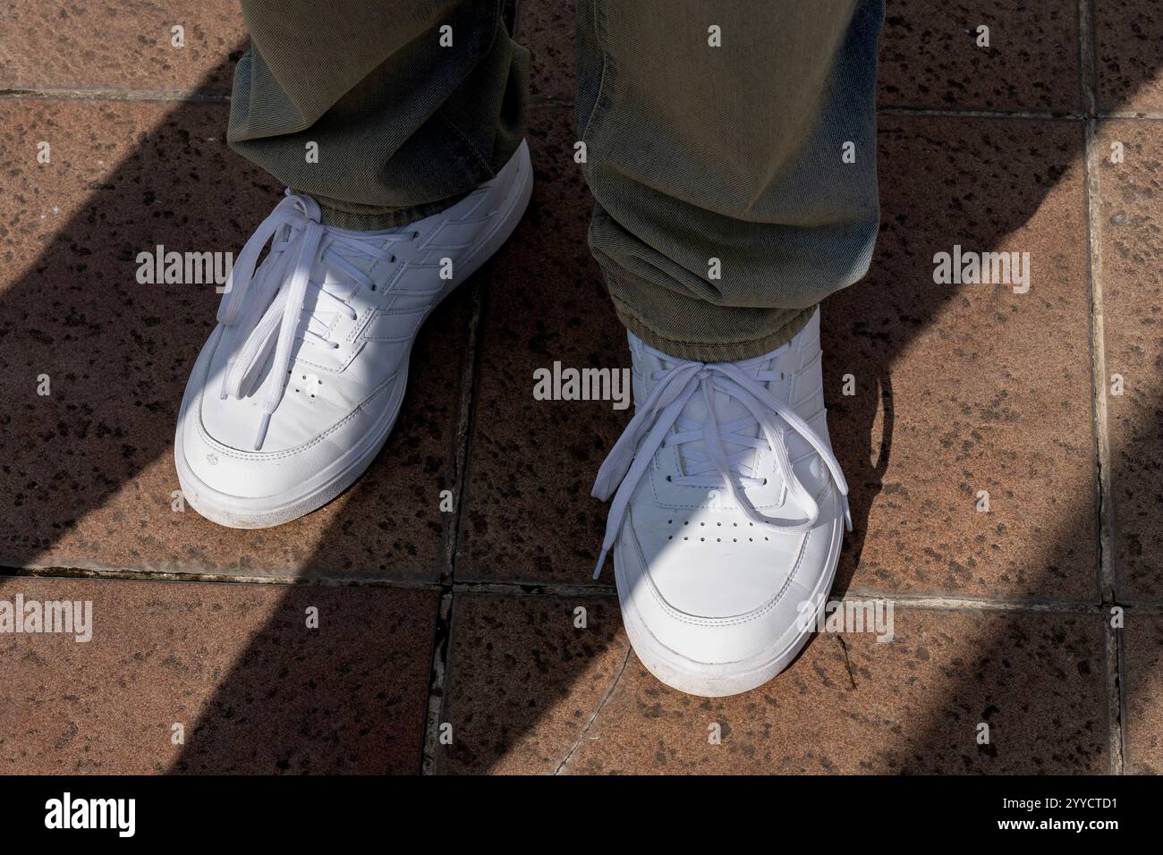 Passi in mezzo al contrasto: Pantaloni verdi e sneakers bianche su pavimento piastrellato Foto Stock