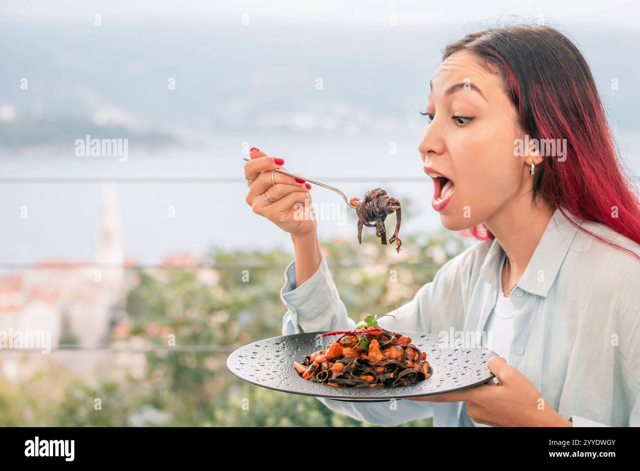 Una donna ama la linguina con frutti di mare, principalmente cozze, in un ristorante che si affaccia sul Mare Adriatico, mescolando delizie culinarie con una vista panoramica sulla costa Foto Stock