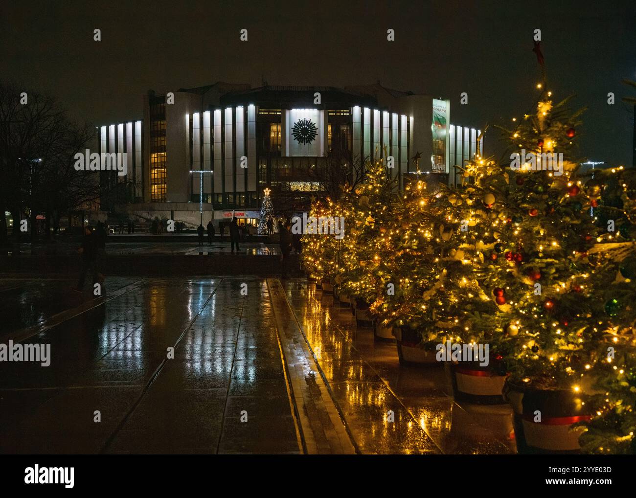 Vista notturna del Palazzo Nazionale della Cultura (NDK) di Sofia, Bulgaria, adornato con le luci natalizie. File di alberi di Natale decorati Foto Stock