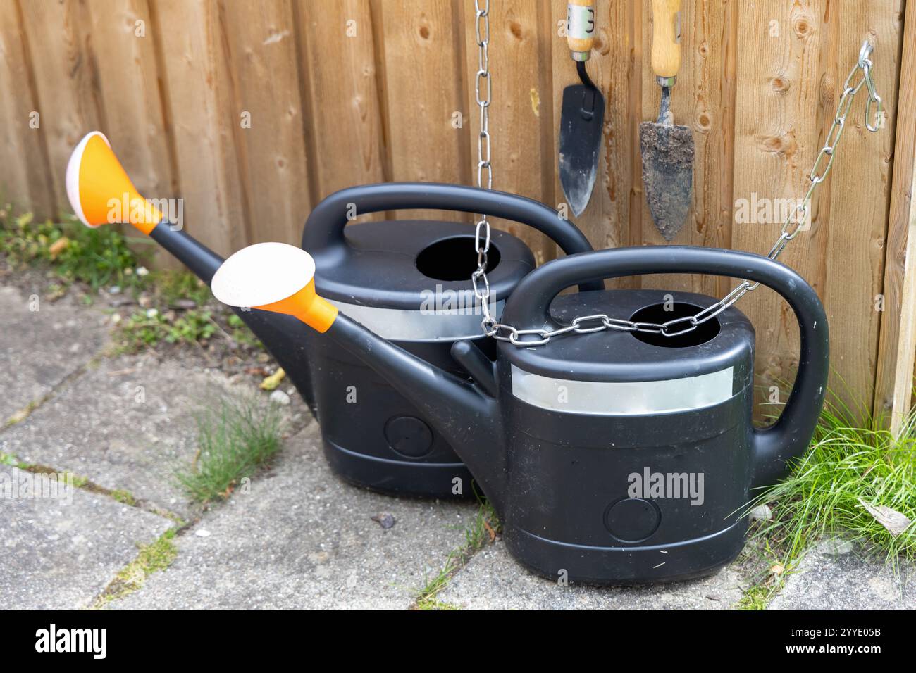 Due lattine nere con punte arancioni accese poggiano su una recinzione in legno rustico, pronte per le attività di giardinaggio Foto Stock