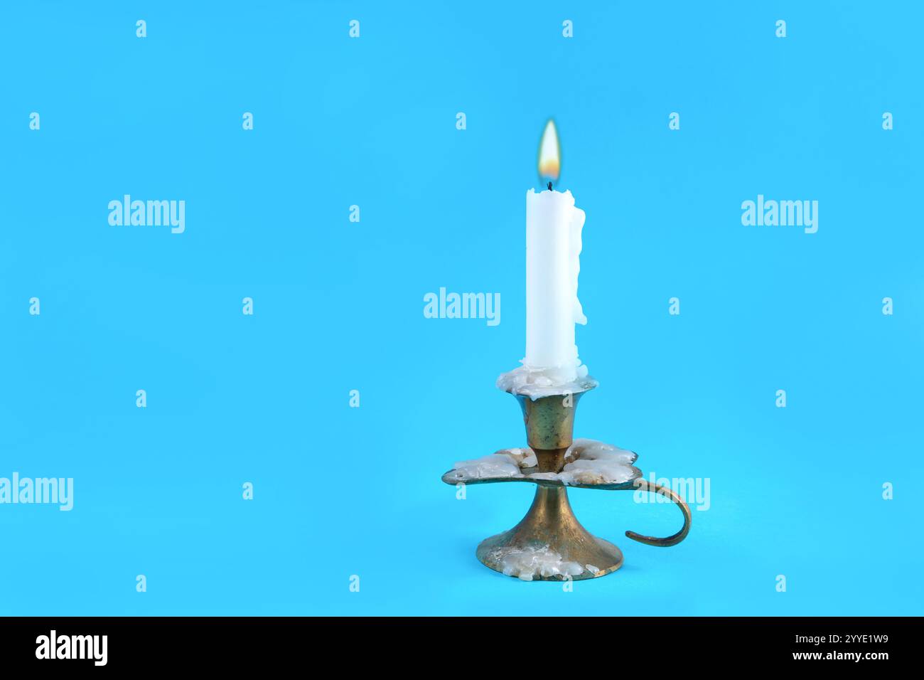 Vecchia candela retrò in un candelabro con una fiamma ardente su un classico sfondo blu in uno studio. Concetto di fuoco e minimalismo con spazio di copia Foto Stock