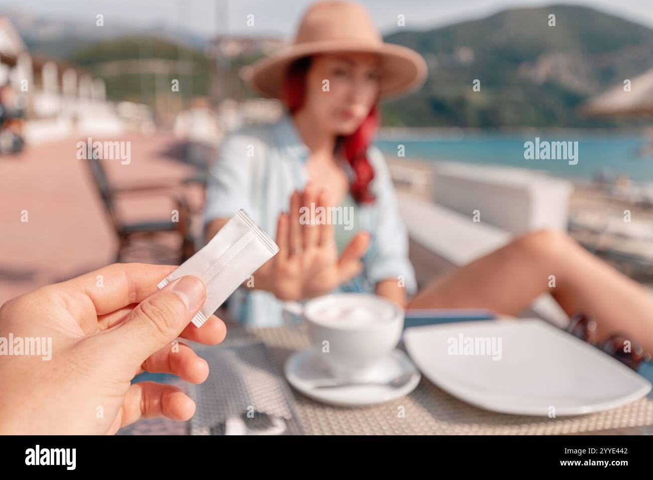 Il turista rifiuta un pacchetto di zucchero in un caffè sulla spiaggia, dando priorità alle scelte attente alla salute mentre si gode la vacanza Foto Stock