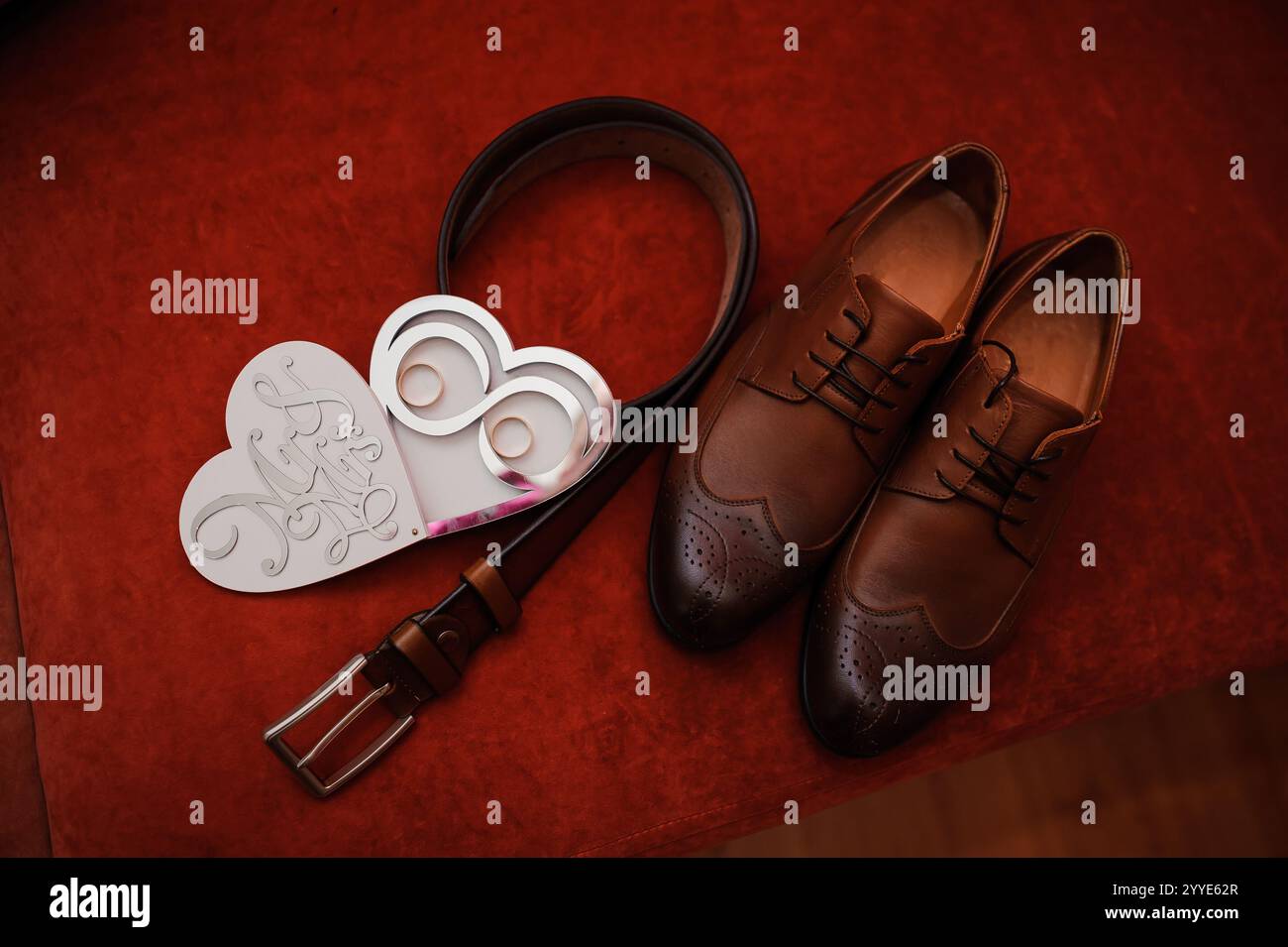 Eleganti scarpe marrone con cintura e carta a forma di cuore su sfondo rosso. Foto Stock