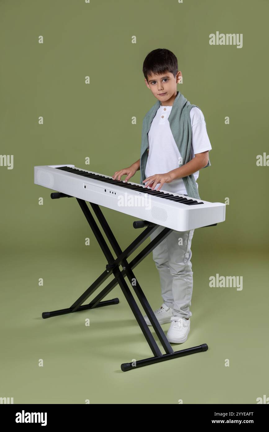 Ragazzo carino che suona sintetizzatore su sfondo verde oliva Foto Stock