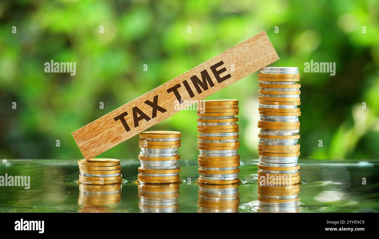 Un blocco di legno con le parole "ORA DELLE TASSE" scritte sopra una pila di monete. Il concetto delle implicazioni finanziarie della stagione fiscale e del potenziale Foto Stock