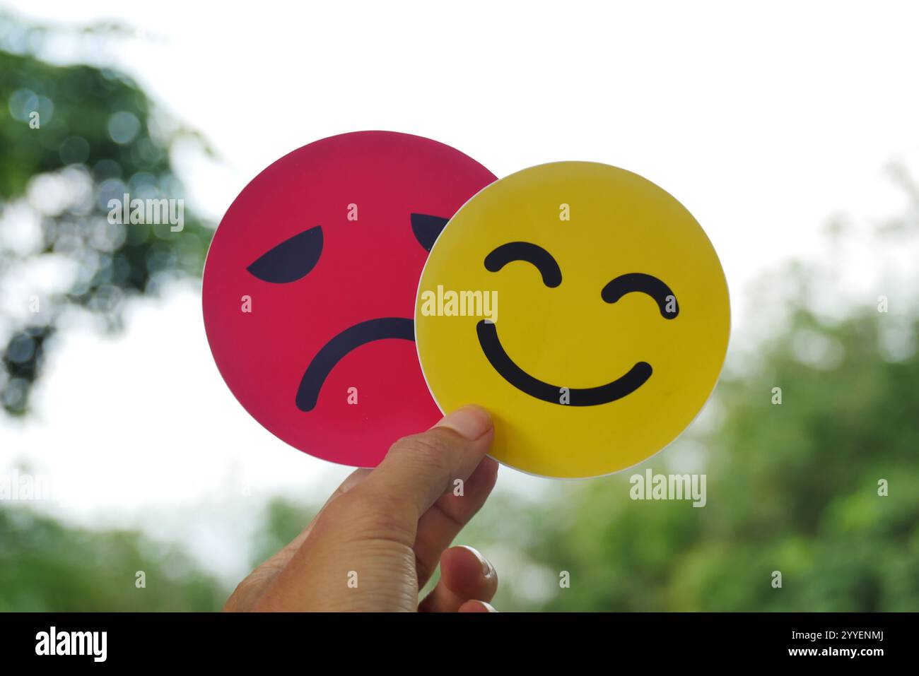 Mano che tiene in mano una triste tessera che si nasconde dietro una faccia felice e sorridente. Concetto bipolare e depressione, concetto di salute mentale, personalità, sbalzi d'umore Foto Stock