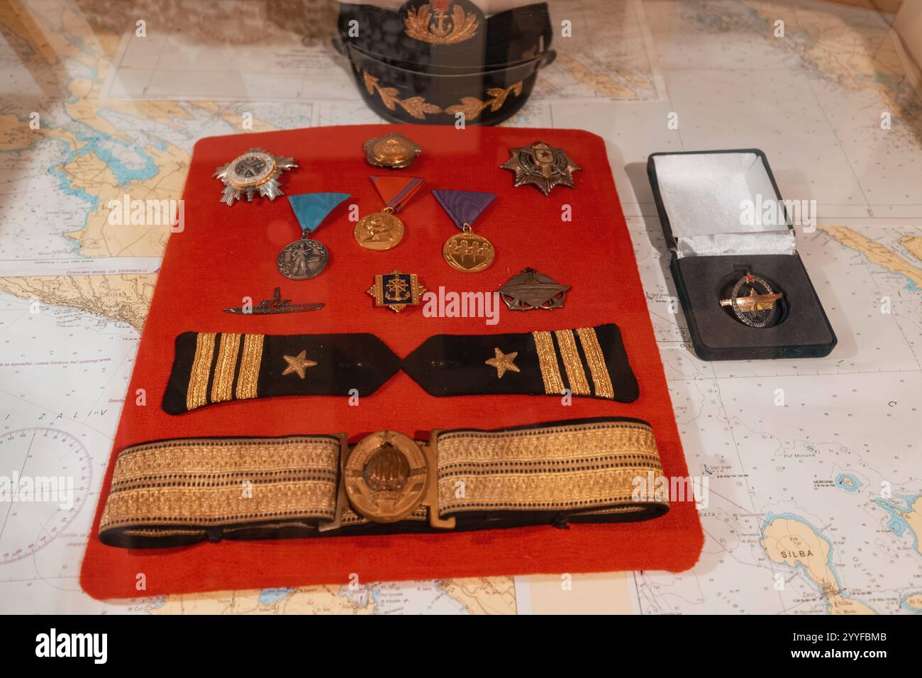 26 ottobre 2024, Tivat, Montenegro: Collezione di accessori, medaglie e distintivi del capitano della marina esposti su un panno rosso con sfondo nautico Foto Stock
