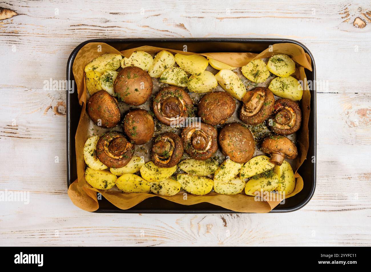 I funghi Champignon e le patate teneri sono conditi con erbe aromatiche e tostati alla perfezione su un vassoio da forno, creando un pasto delizioso Foto Stock