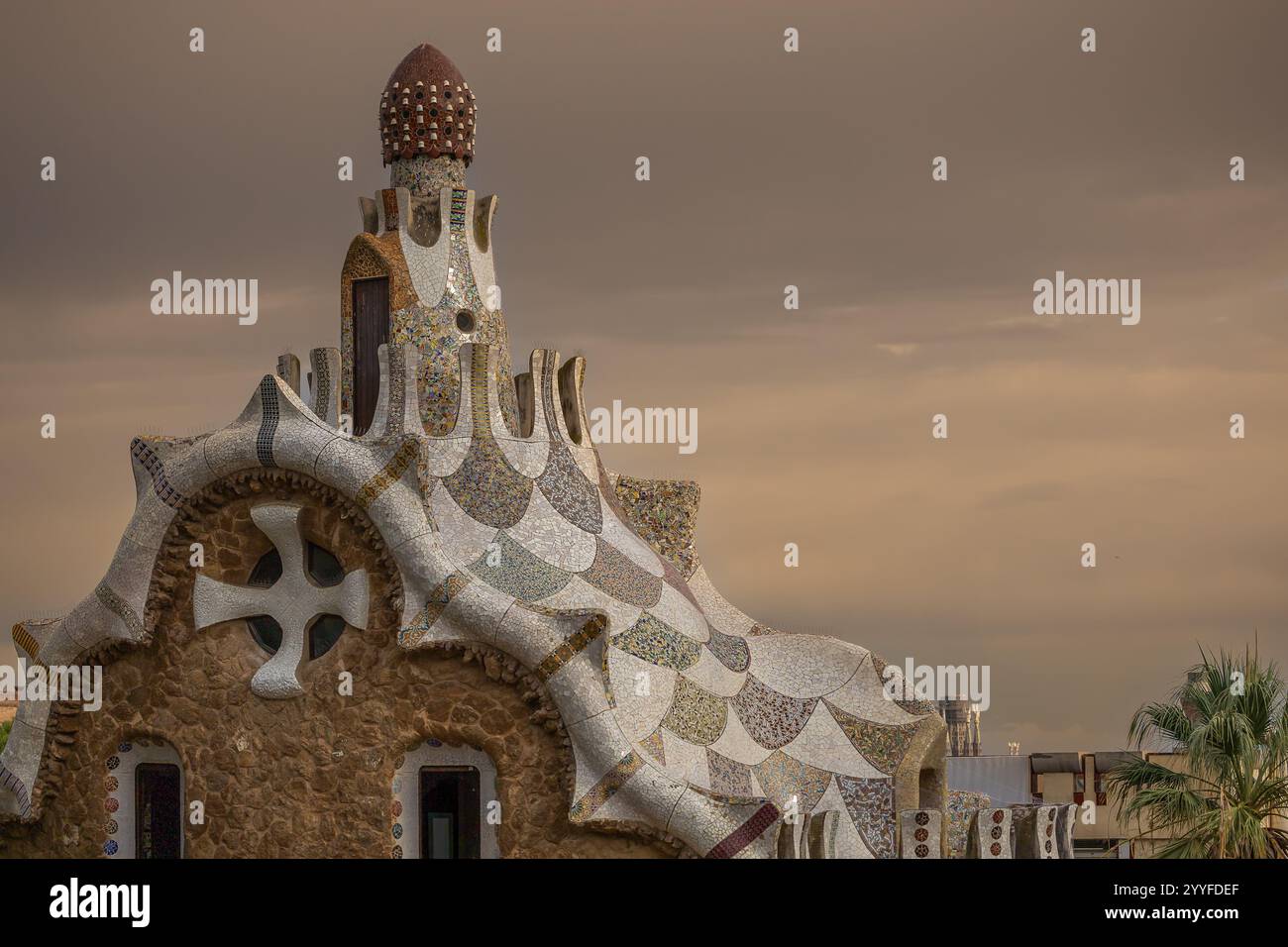 Iconico edificio progettato da Gaudí a Park Güell, Barcellona, che presenta intricati dettagli a mosaico sotto un cielo coperto di moody Foto Stock