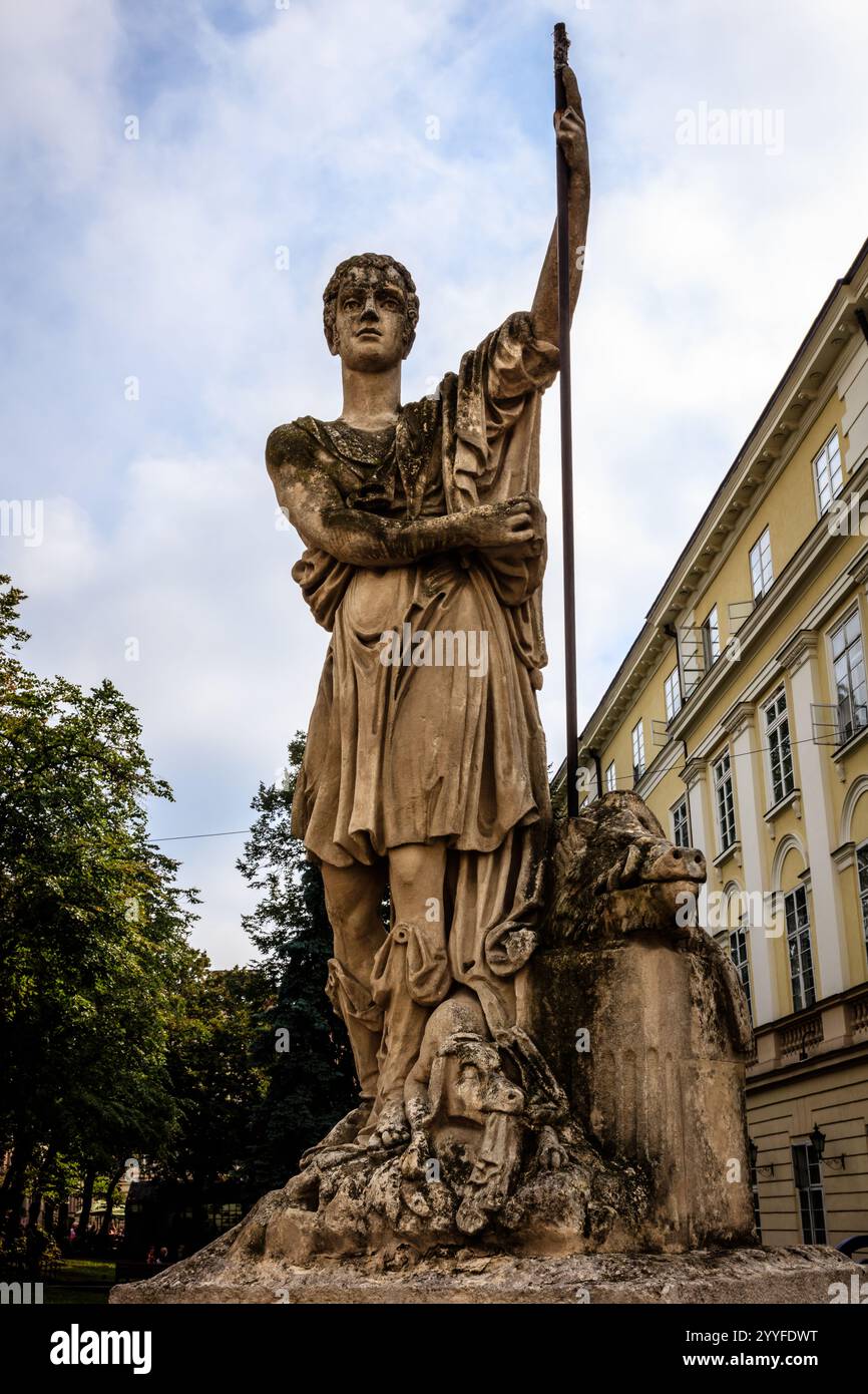 Una statua di un uomo con una lancia è in piedi di fronte a un edificio. La statua è fatta di pietra e ha un aspetto molto antico e intempestivo. Il bui Foto Stock