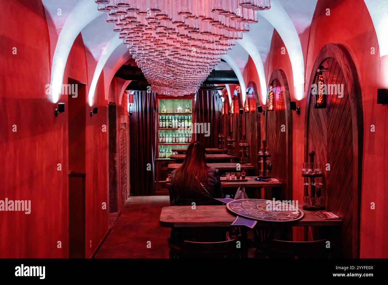 Una sala rossa con un lampadario e una persona seduta a un tavolo. La sala è poco illuminata e presenta un'atmosfera intima Foto Stock