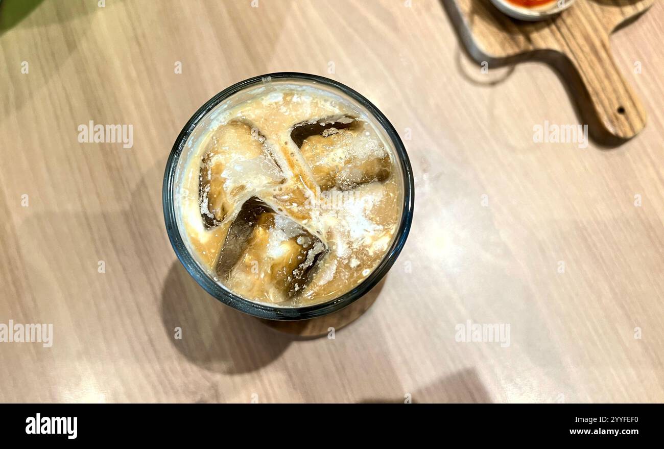 Vista aerea ravvicinata del caffè di ghiaccio con latte e cubetti di ghiaccio sul bicchiere. Il caffè Ice Palm Sugar Milk è molto popolare in Indonesia da adolescenti e offi Foto Stock