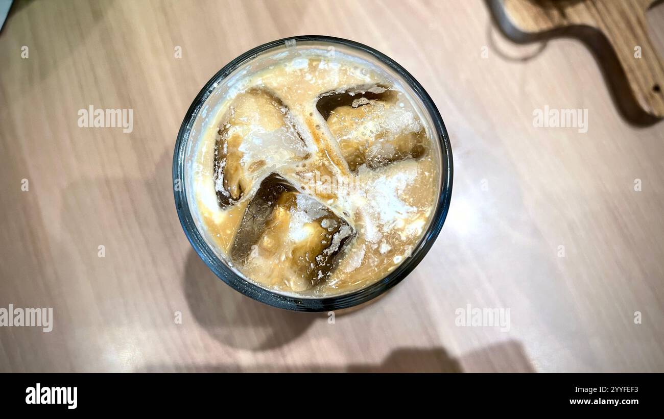 Vista aerea ravvicinata del caffè di ghiaccio con latte e cubetti di ghiaccio sul bicchiere. Il caffè Ice Palm Sugar Milk è molto popolare in Indonesia da adolescenti e offi Foto Stock