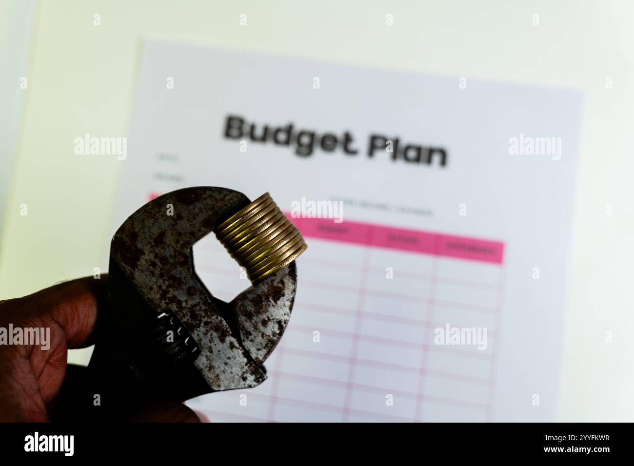 Tagli al bilancio, pressioni finanziarie e difficoltà economiche simboleggiate da monete schiacciate in una chiave inglese. Foto Stock