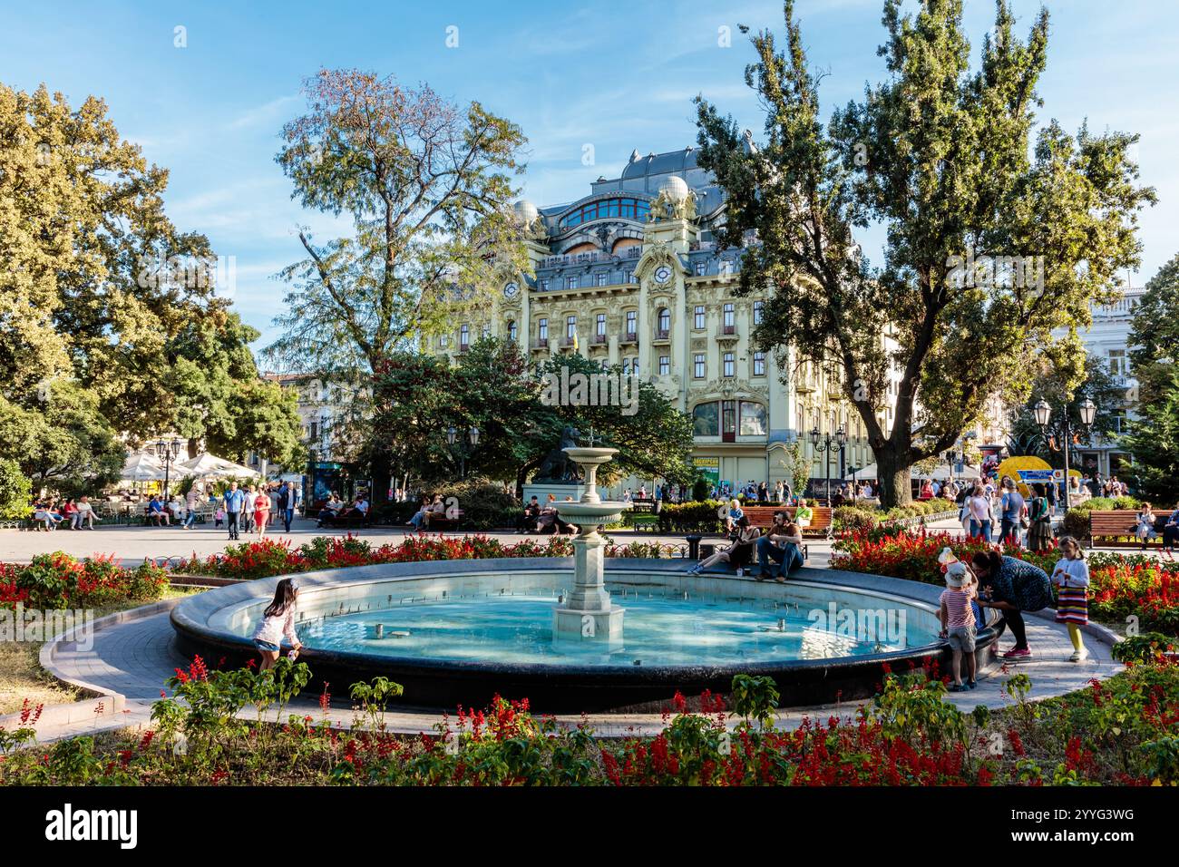 Una grande fontana in un parco con un edificio sullo sfondo. Le persone sono sedute sulle panchine e si godono la vista Foto Stock