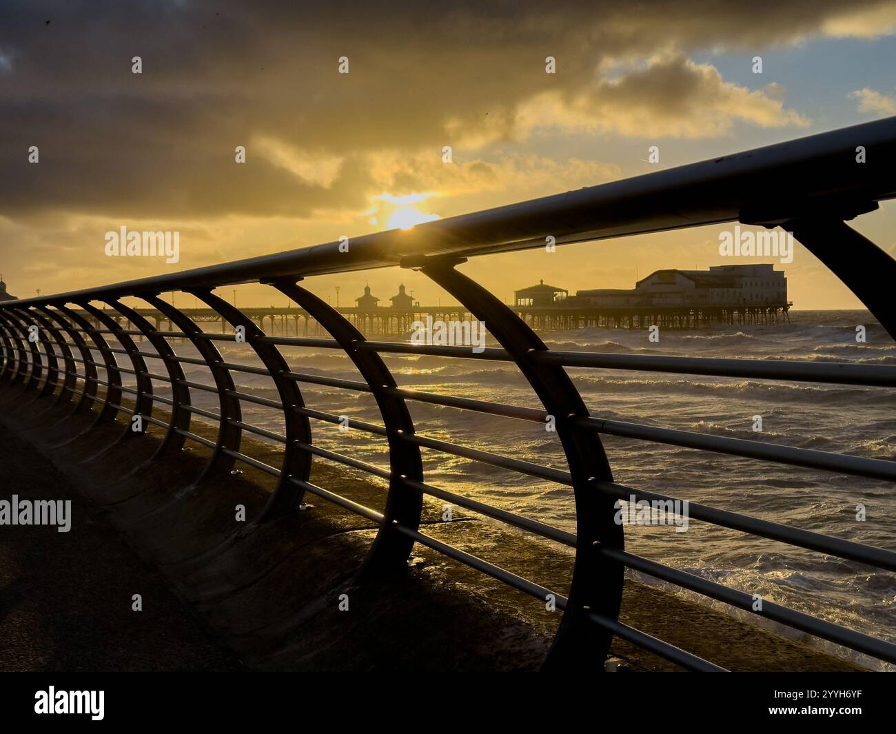 Il molo centrale di Blackpool si vede attraverso la barriera sulla passeggiata illuminata dalla luce del sole invernale serale Foto Stock
