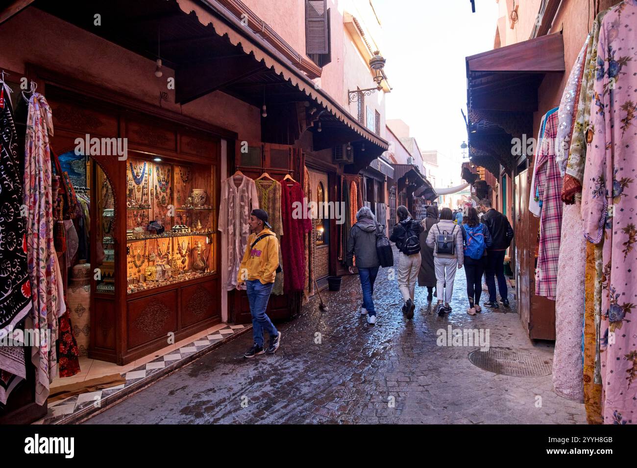 i turisti camminano davanti ai negozi e attraverso la vecchia strada bagnata della medina di marrakech, in marocco Foto Stock