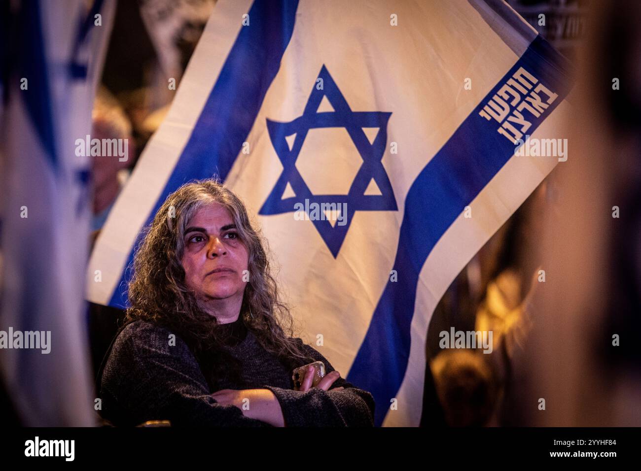 Una donna israeliana si trova accanto alla bandiera israeliana durante una protesta a Tel Aviv sabato 21 dicembre 2024. Sabato, migliaia di persone sono scese per le strade di Israele chiedendo all'attuale governo guidato dal primo ministro Benjamin Netanyahu di raggiungere un accordo con Hamas. Foto di Eyal Warshavsky. Foto Stock