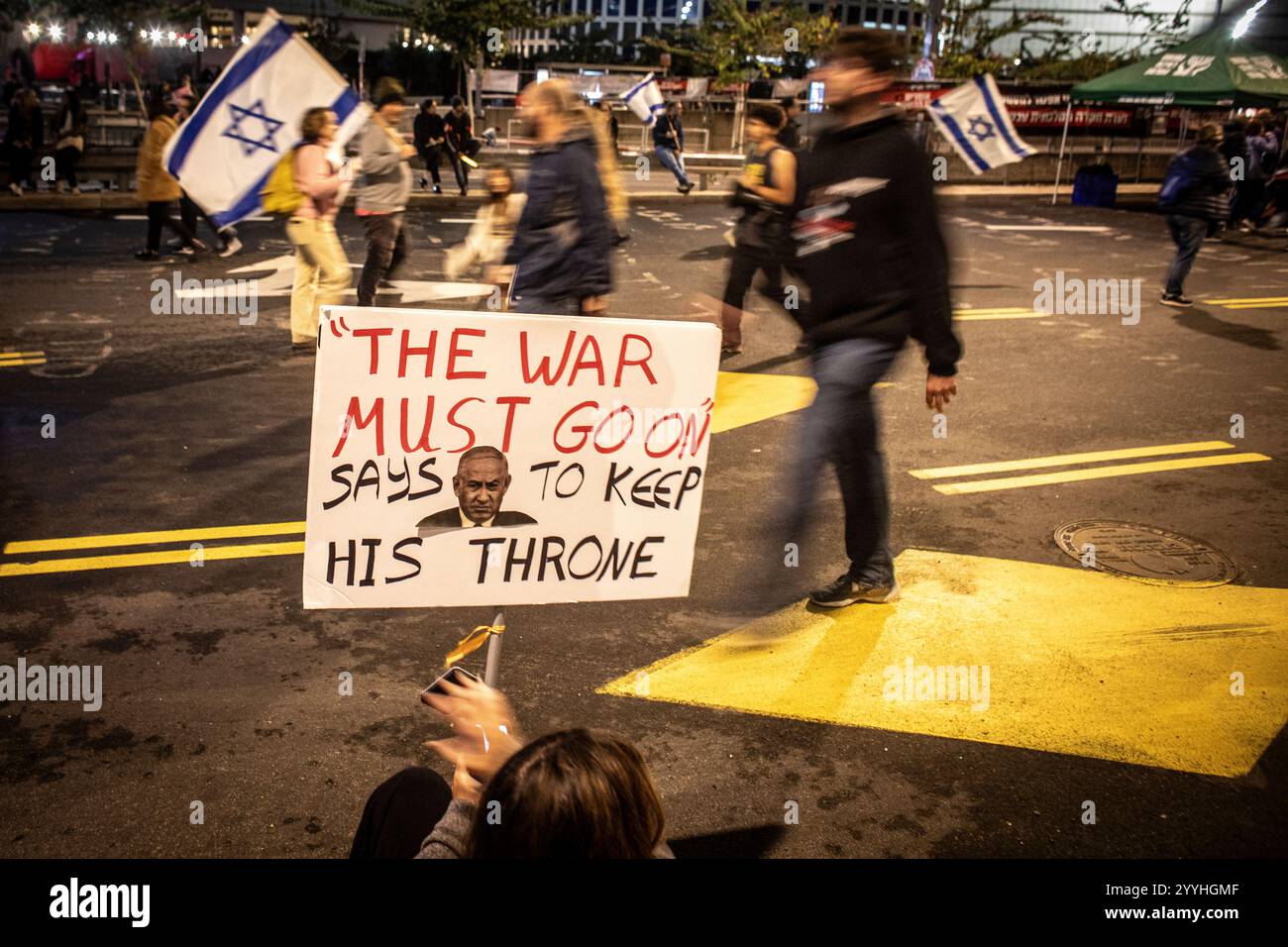 Gli israeliani passano davanti a una donna con un cartello anti Netanyahu durante una protesta a Tel Aviv sabato 21 dicembre 2024. Sabato, migliaia di persone sono scese per le strade di Israele chiedendo all'attuale governo guidato dal primo ministro Benjamin Netanyahu di raggiungere un accordo con Hamas. Foto di Eyal Warshavsky. Foto Stock