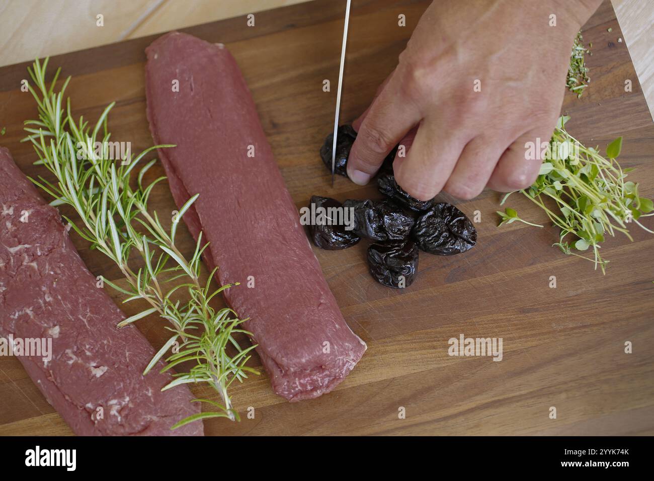 Cucina sveva, preparazione di agnello con prugne, agnello crudo, rosmarino, erbe aromatiche, aglio a fette, scorza di limone, filetti su tavola di legno, prugne da taglio, cuciture Foto Stock