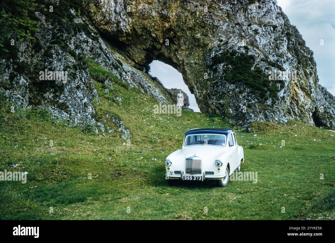 Foto storica di una donna in piedi sotto un arco naturale e di un'auto Morris Alvis parcheggiata sull'erba di fronte negli anni '1960, Scottish Highlands, Scozia, Regno Unito Foto Stock