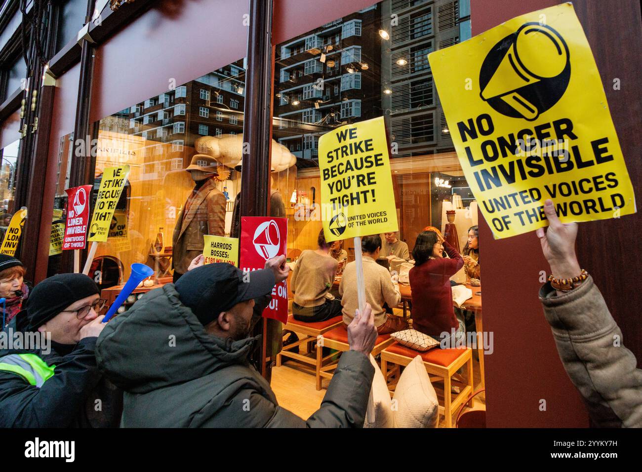 Londra, Regno Unito. 21 dicembre 2024. I lavoratori Harrods, rappresentati dal sindacato United Voices of the World (UVW), cercano di attirare l'attenzione dei clienti che partecipano a un'officina all'interno dei grandi magazzini di lusso. I membri dell'UVW, che fanno le pulizie notturne, prevalentemente lavoratori migranti, stanno intraprendendo azioni industriali contro una nuova politica di congedo Harrods che limita gravemente la loro capacità di prendersi un periodo di ferie per visitare le loro famiglie all'estero. Alla linea esterna del picchetto erano presenti anche le guardie di sicurezza UVW del Museo della Scienza, del Museo di storia naturale e del Victoria & Albert Museum Foto Stock