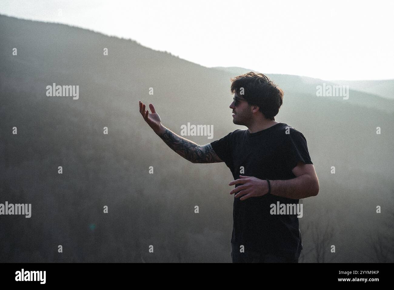 In un'accattivante foto in bianco e nero, un uomo vestito con una camicia nera si trova di fronte a un maestoso sfondo di montagna Foto Stock