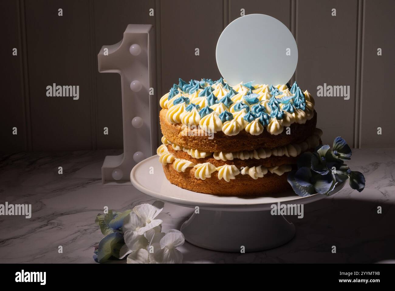 Una torta del primo compleanno con spazio per il testo su un disco sopra la torta. Un singolo numero è sulla tavolozza a lato. una torta bianca. Foto Stock