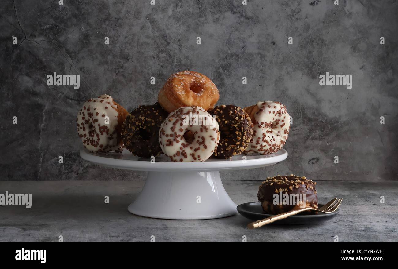 Un banco per torte con un'ampia selezione di piccole ciambelle decorate, un piatto laterale contiene una ciambella a scelta con una forchetta d'oro. Foto Stock