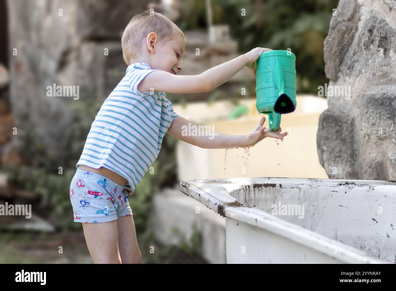 Un ragazzo gioca con una bomboletta per innaffiare in giardino Foto Stock