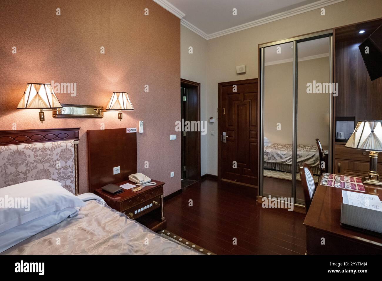 Una camera da letto con letto, comodino e lampada. La camera era pulita e ben illuminata, con uno specchio sul muro Foto Stock