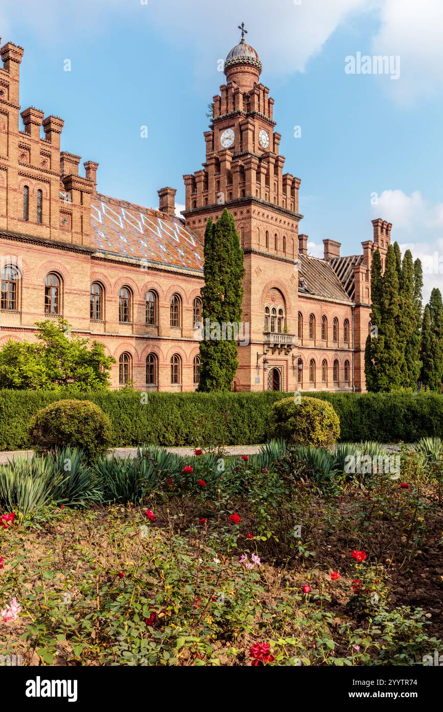 Un grande edificio in mattoni con una torre dell'orologio e un cortile con fiori. L'edificio è vecchio e ha molta storia Foto Stock