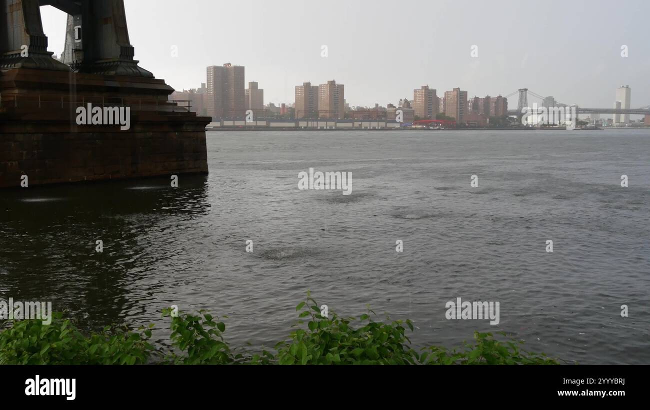 Piovosa New York sotto il ponte di Manhattan a Brooklyn. Passeggiata sul lungomare di Dumbo, East River. Meteo Foggy Day sul lungofiume sotto il ponte. Pioggia e acqua fluviale. Cadute sull'obiettivo della fotocamera. Foto Stock