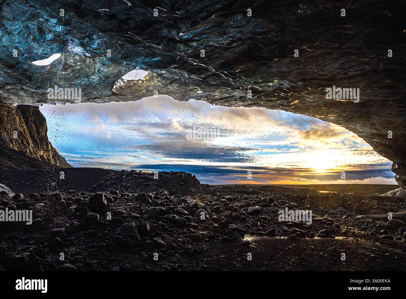 Una vista mozzafiato dall'interno di una grotta di ghiaccio mostra vivaci sfumature del cielo e terreni accidentati al tramonto. La luce del sole proietta bellissime ombre sulla lan Foto Stock
