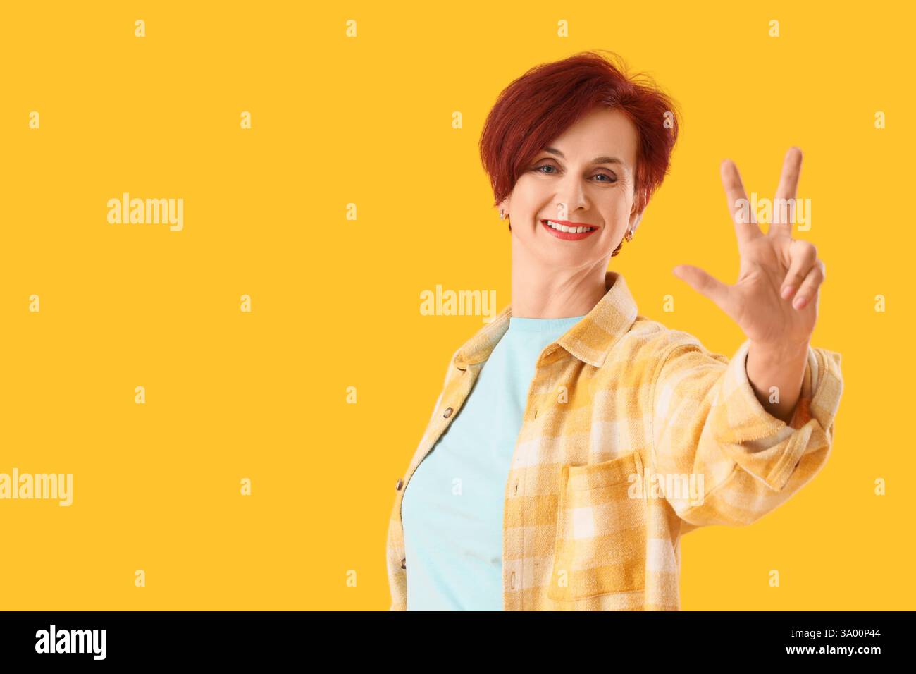 Donna matura che mostra tre dita su sfondo giallo. Concetto di regole Foto Stock