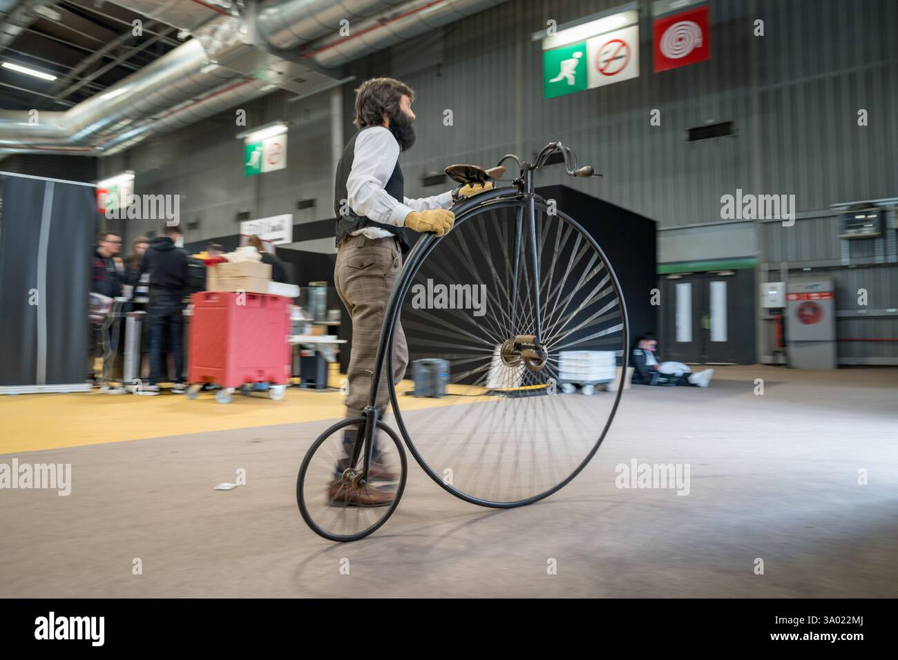 Il ciclista d'epoca naviga nella grande sala espositiva mostrando creatività e tradizioni uniche durante un vivace evento che celebra l'artigianato Foto Stock