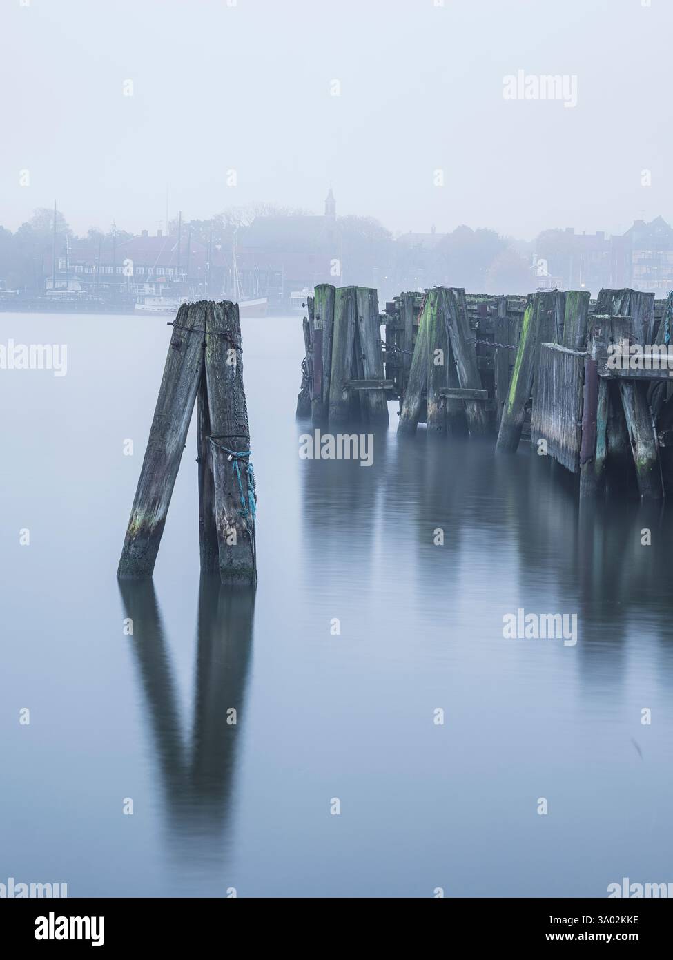 Le acque calme avvolgono le vecchie colonne di legno del porto di Goteborg, avvolte da una leggera nebbia durante le prime ore del mattino, creando un ambiente sereno e rilassante Foto Stock