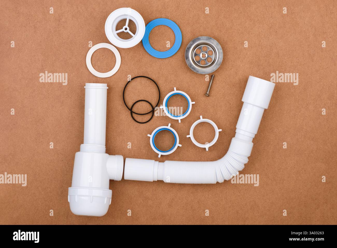 Kit complessivo scarico lavello completo completamente disassemblato, comprensivo di tubo flessibile, guarnizioni, filtro a rete e vari connettori disposti su una superficie marrone. Foto Stock