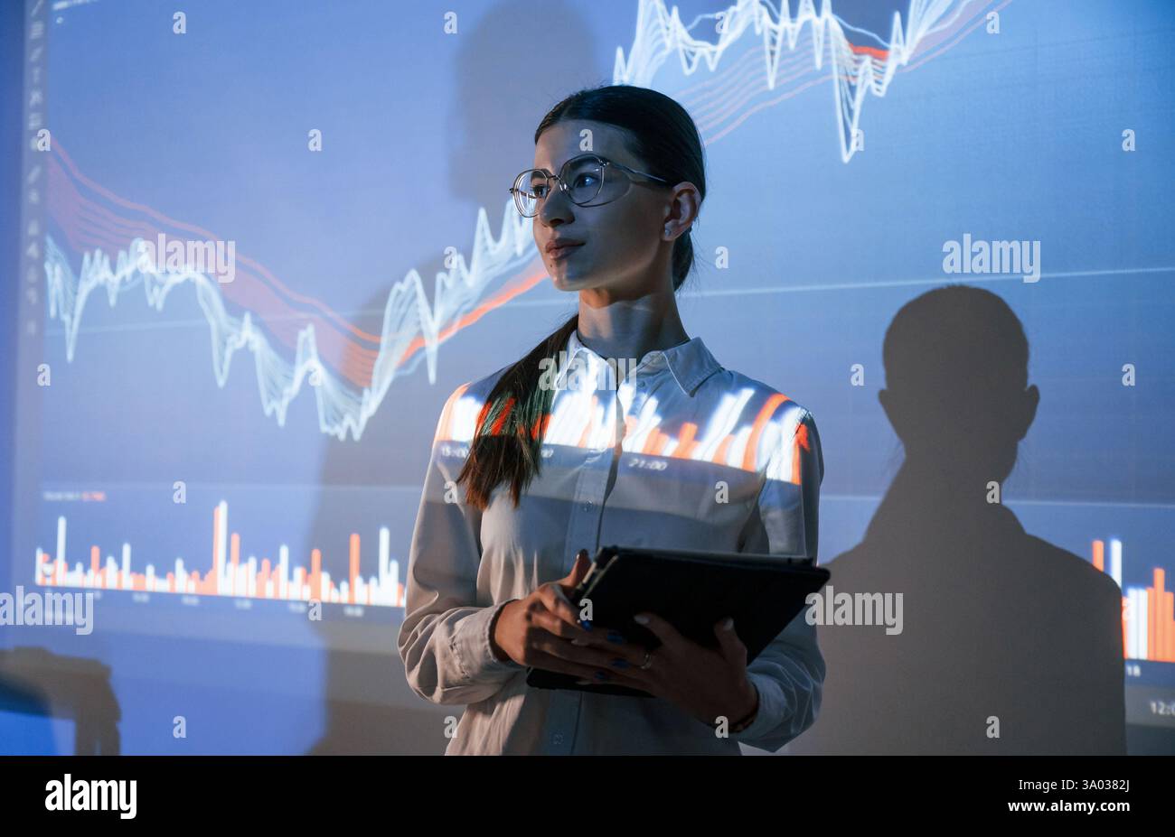 La donna è in piedi vicino al proiettore con i grafici finanziari. Foto Stock