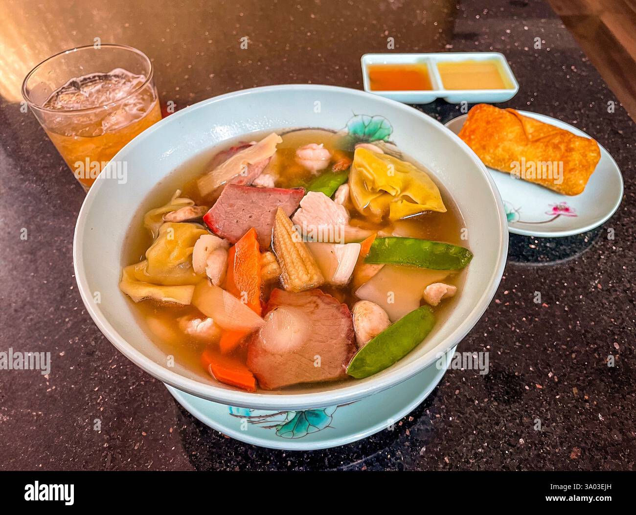 Una deliziosa ciotola di zuppa di wonton ripiena di gnocchi, maiale barbecue, pollo, gamberi e verdure fresche. Servito con un involtino d'uovo, salse per immersione e un re Foto Stock